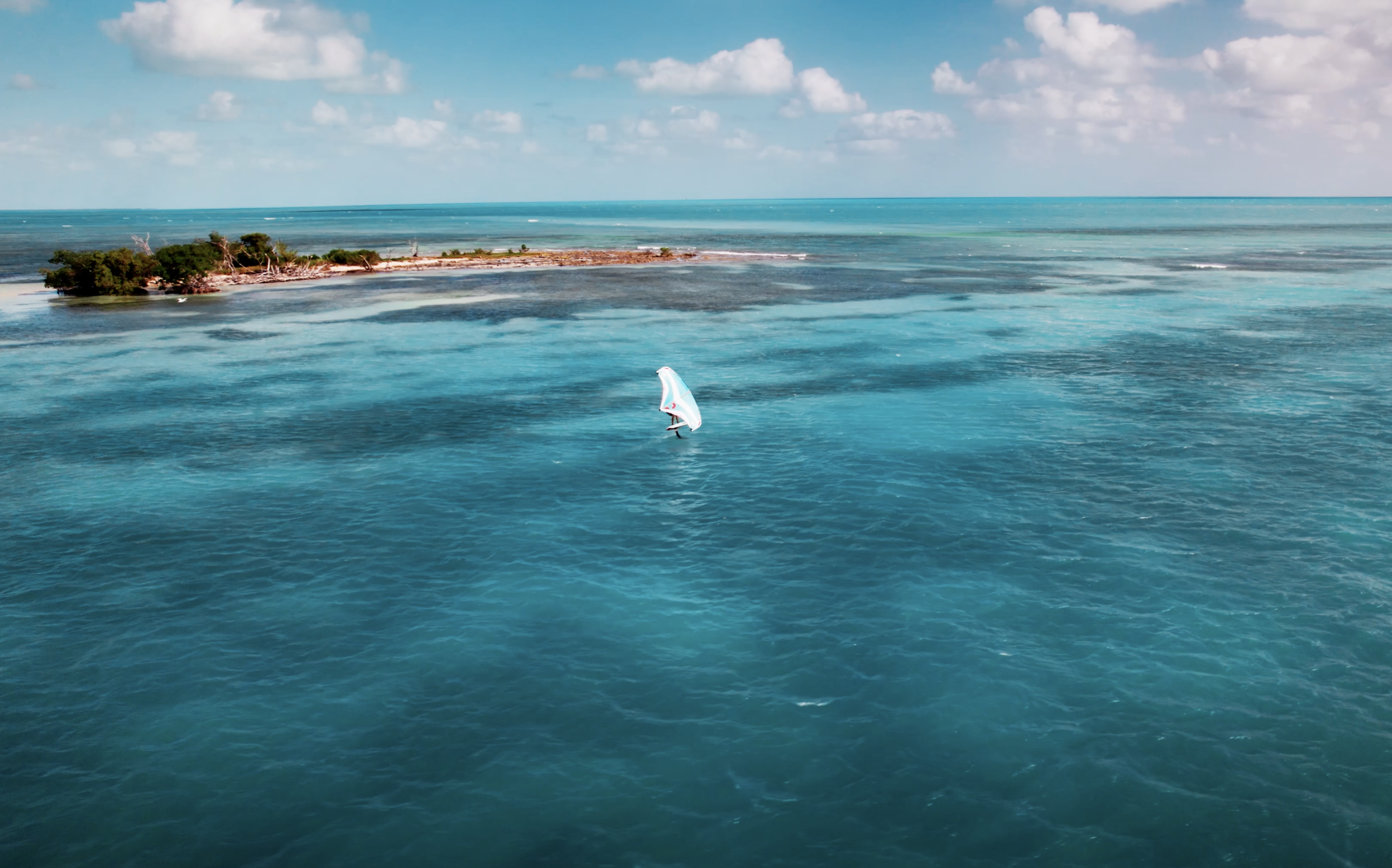 Sailboat on open blue water with an island backdrop – Florida Keys Videography & Photography